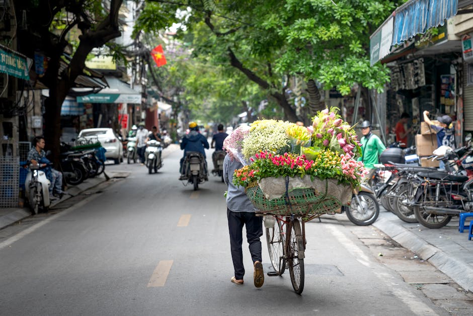 A street scene in Nevern Place and Earls Court SW5 showing a flower delivery person walking down the road pushing a bicycle with an oversized basket filled with fresh, vibrant flowers, including pink,
